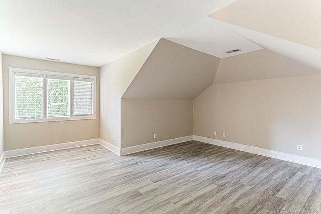 bonus room featuring baseboards, lofted ceiling, light wood-type flooring, and visible vents