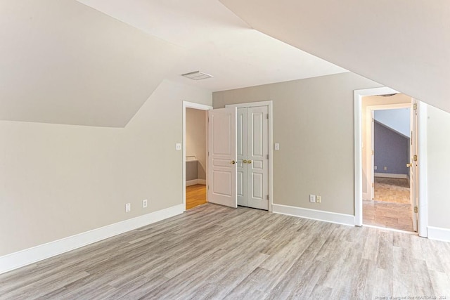 additional living space with light wood-type flooring, baseboards, lofted ceiling, and visible vents