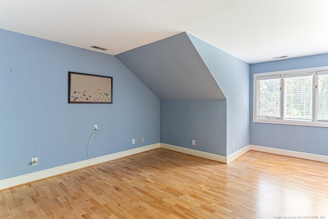 bonus room with baseboards, lofted ceiling, light wood-type flooring, and visible vents
