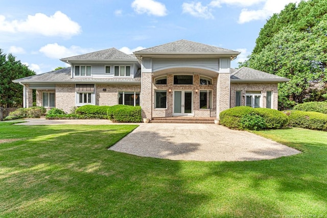 rear view of property featuring a lawn, a shingled roof, french doors, and brick siding