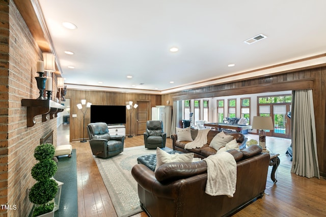 living room featuring wooden walls, wood-type flooring, crown molding, a brick fireplace, and brick wall