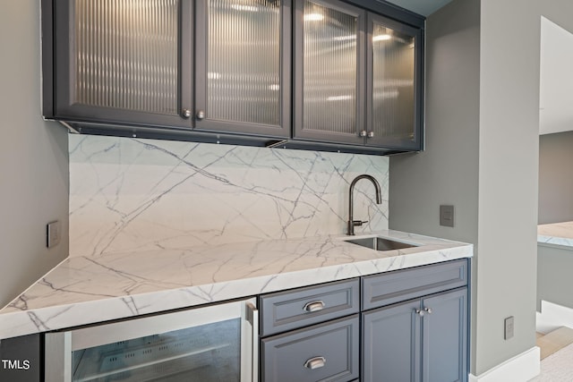 kitchen featuring light stone counters, beverage cooler, a sink, and backsplash