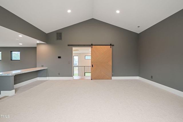 spare room featuring light carpet, a barn door, visible vents, baseboards, and lofted ceiling