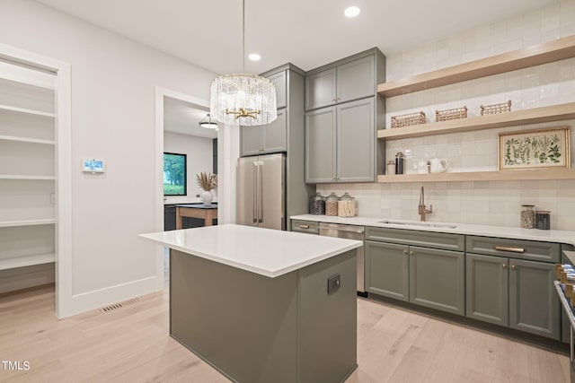 kitchen featuring stainless steel appliances, a sink, hanging light fixtures, light countertops, and open shelves