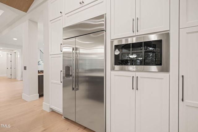 kitchen with light wood-style flooring, baseboards, white cabinets, and built in appliances