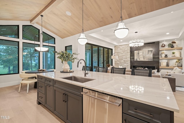 kitchen with hanging light fixtures, stainless steel dishwasher, open floor plan, a sink, and light stone countertops