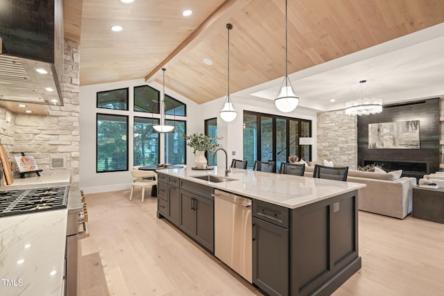 kitchen featuring light stone counters, open floor plan, decorative light fixtures, a sink, and stainless steel dishwasher