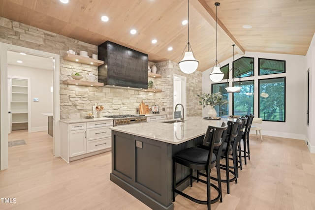 kitchen with open shelves, hanging light fixtures, white cabinets, a sink, and wall chimney exhaust hood