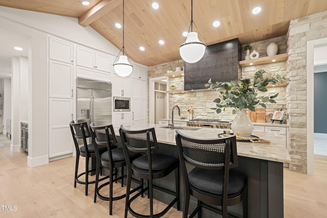 kitchen featuring built in appliances, a sink, white cabinetry, light stone countertops, and decorative light fixtures