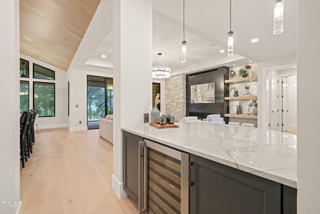 kitchen featuring wine cooler, light stone counters, decorative light fixtures, light wood-style floors, and open shelves