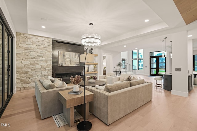 living area featuring stairway, a tray ceiling, light wood-style floors, a fireplace, and a chandelier