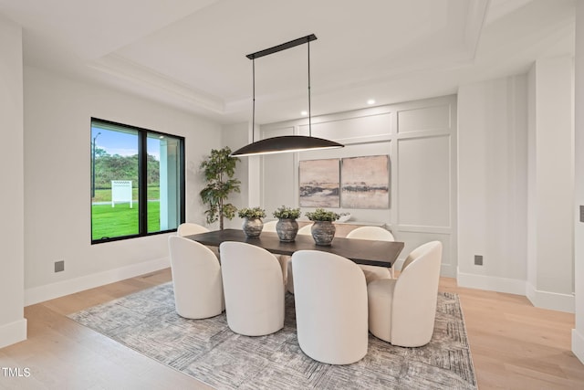 dining space with baseboards, a tray ceiling, and light wood-style floors