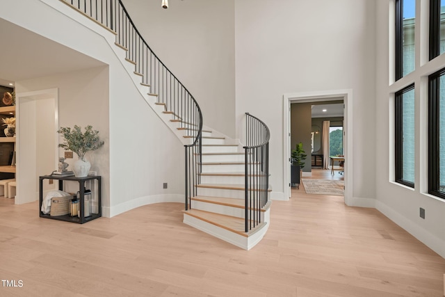 foyer with a towering ceiling, light wood-style flooring, stairway, and baseboards