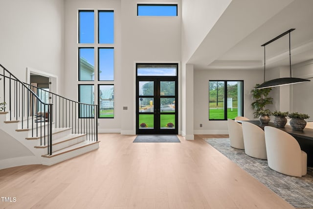 foyer featuring baseboards, a towering ceiling, stairway, wood finished floors, and french doors