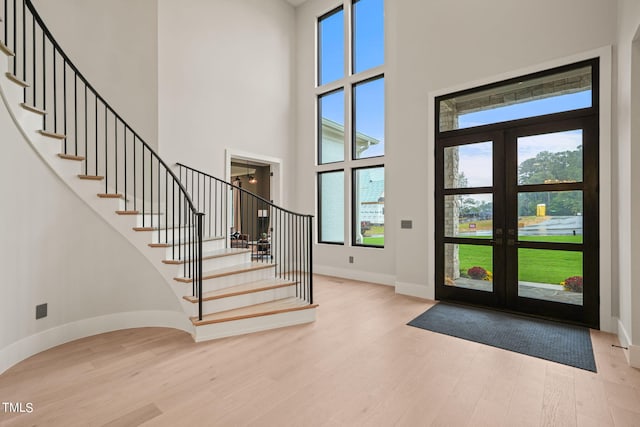 entryway featuring baseboards, a towering ceiling, light wood-style flooring, stairs, and french doors