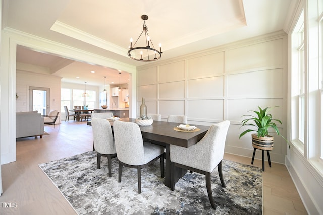 dining area featuring light hardwood / wood-style floors, a raised ceiling, crown molding, and a notable chandelier