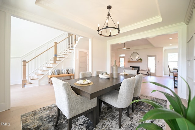 dining area with a raised ceiling, ceiling fan with notable chandelier, light hardwood / wood-style floors, and ornamental molding