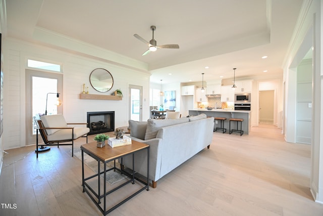 living room with ceiling fan, light hardwood / wood-style flooring, and a tray ceiling