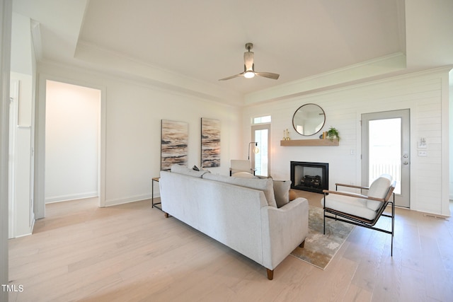 living room featuring ceiling fan, a raised ceiling, and light hardwood / wood-style flooring