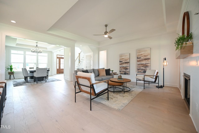 living room with ceiling fan with notable chandelier, light hardwood / wood-style flooring, crown molding, and a raised ceiling