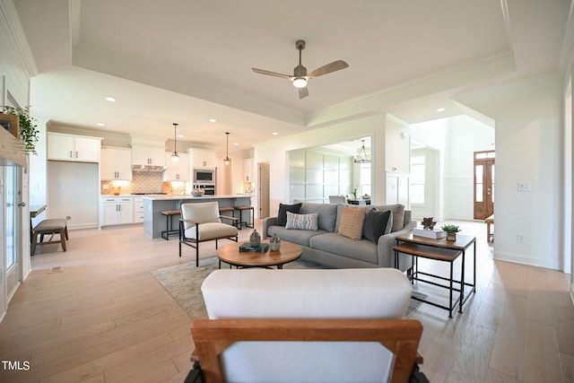 living room with ceiling fan, light hardwood / wood-style flooring, ornamental molding, and a tray ceiling