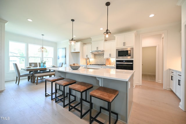 kitchen featuring light wood-type flooring, backsplash, an island with sink, black oven, and stainless steel microwave