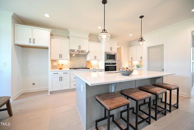 kitchen featuring a kitchen breakfast bar, decorative backsplash, a kitchen island with sink, stainless steel appliances, and white cabinets