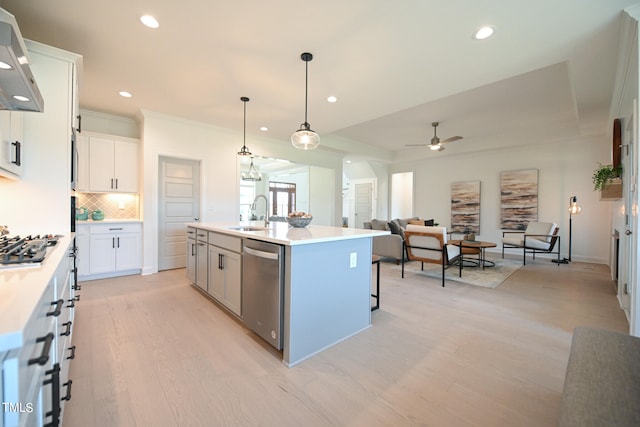 kitchen with stainless steel appliances, light hardwood / wood-style floors, white cabinetry, a center island with sink, and wall chimney range hood