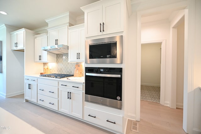 kitchen featuring appliances with stainless steel finishes, white cabinetry, light wood-type flooring, and tasteful backsplash