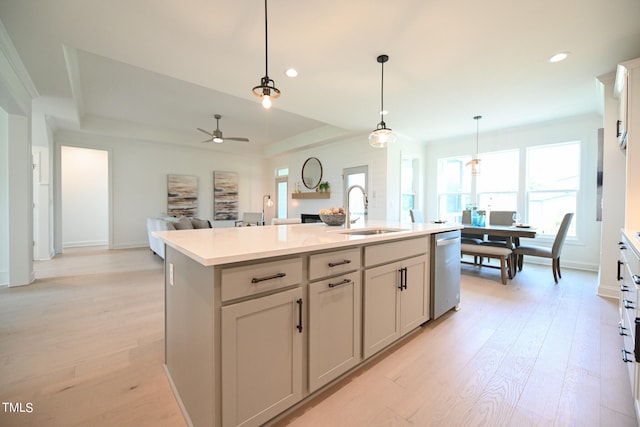 kitchen with light hardwood / wood-style flooring, a kitchen island with sink, stainless steel dishwasher, and hanging light fixtures