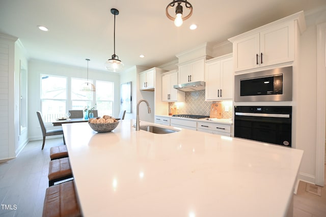 kitchen featuring appliances with stainless steel finishes, white cabinetry, tasteful backsplash, sink, and an island with sink