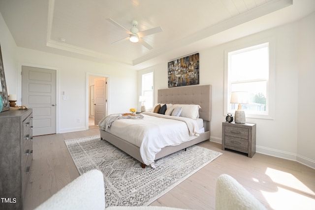 bedroom featuring light hardwood / wood-style floors, a raised ceiling, ceiling fan, and multiple windows