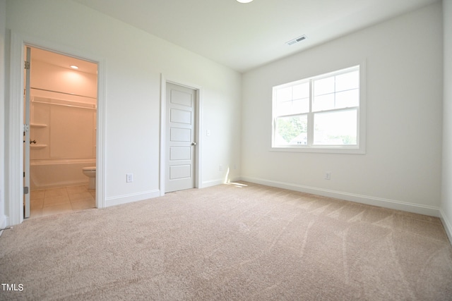 unfurnished bedroom featuring a closet, light colored carpet, and ensuite bathroom