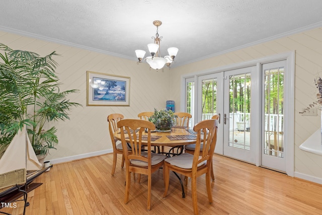 dining room with a textured ceiling, a notable chandelier, light wood-type flooring, crown molding, and french doors