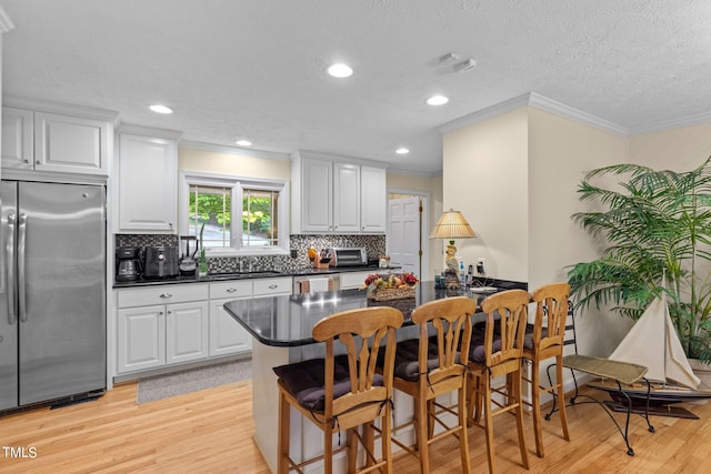 kitchen featuring white cabinets, light hardwood / wood-style flooring, stainless steel appliances, a breakfast bar area, and tasteful backsplash