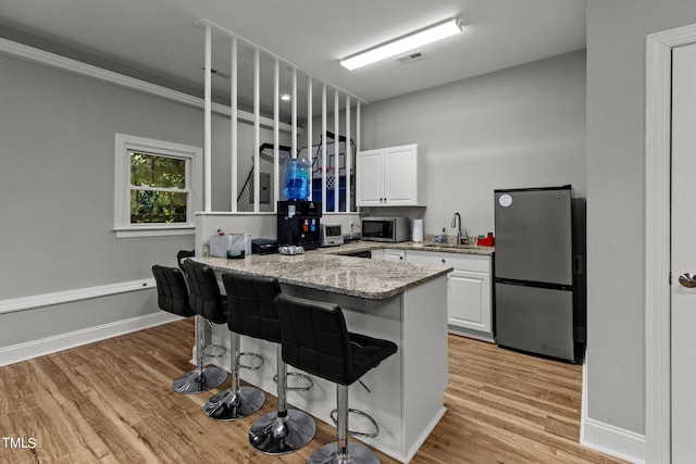 kitchen with light stone countertops, light hardwood / wood-style flooring, stainless steel appliances, white cabinets, and sink