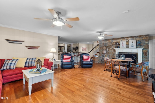 living room with wood-type flooring, ornamental molding, ceiling fan, and a stone fireplace