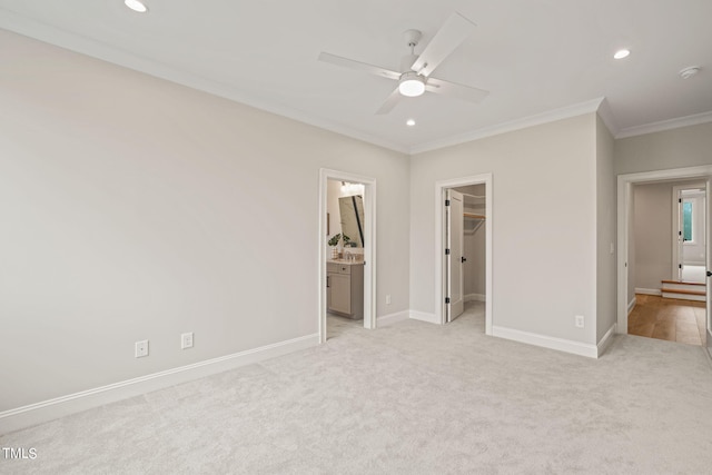 unfurnished bedroom with ceiling fan, connected bathroom, a walk in closet, light colored carpet, and crown molding