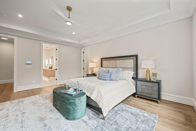 bedroom featuring light hardwood / wood-style flooring, connected bathroom, a tray ceiling, and ceiling fan