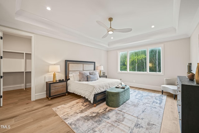 bedroom with light hardwood / wood-style flooring, a tray ceiling, and a walk in closet