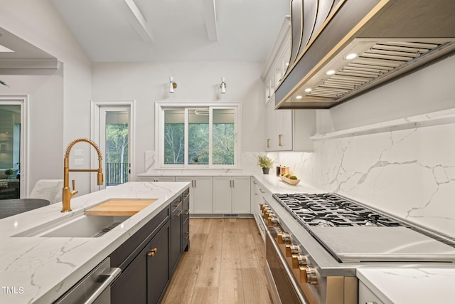 kitchen featuring appliances with stainless steel finishes, custom range hood, light hardwood / wood-style floors, white cabinets, and sink