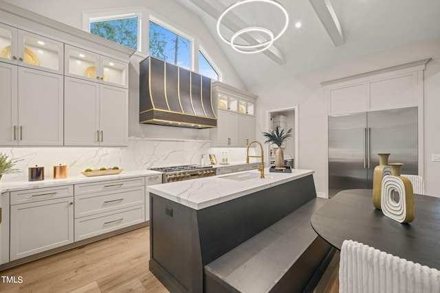 kitchen featuring custom exhaust hood, lofted ceiling, sink, appliances with stainless steel finishes, and light wood-type flooring