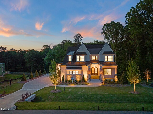 view of front of house with stone siding, stucco siding, curved driveway, a front lawn, and a standing seam roof