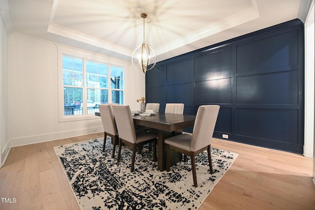 dining area with a chandelier, a raised ceiling, light hardwood / wood-style flooring, and ornamental molding