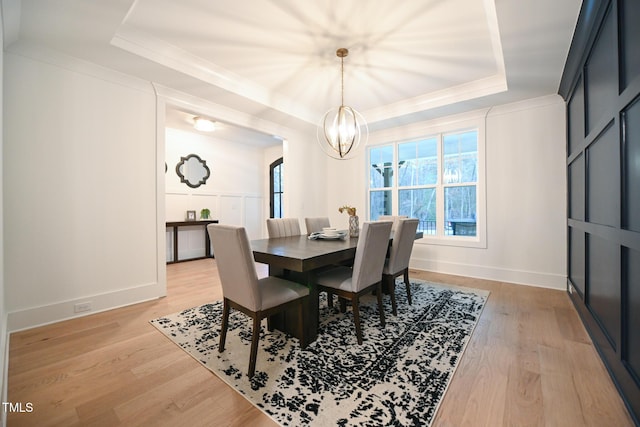 dining space with a raised ceiling, light hardwood / wood-style floors, and a notable chandelier