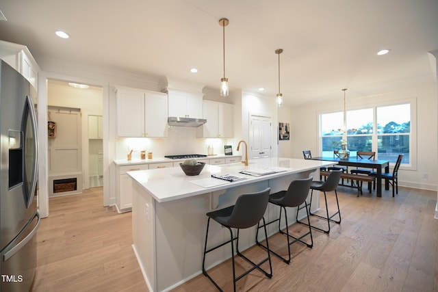 kitchen featuring white cabinetry, stainless steel fridge with ice dispenser, a center island with sink, and decorative light fixtures