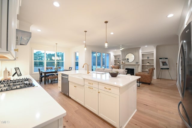 kitchen featuring white cabinetry, a large fireplace, hanging light fixtures, a kitchen island with sink, and appliances with stainless steel finishes