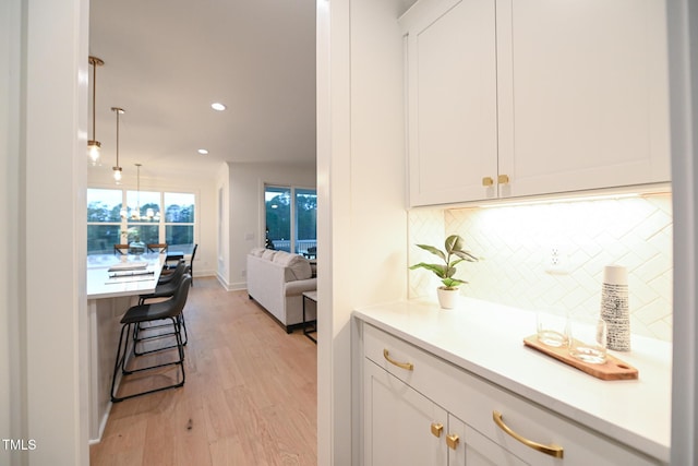 interior space with tasteful backsplash, white cabinetry, light hardwood / wood-style flooring, and decorative light fixtures