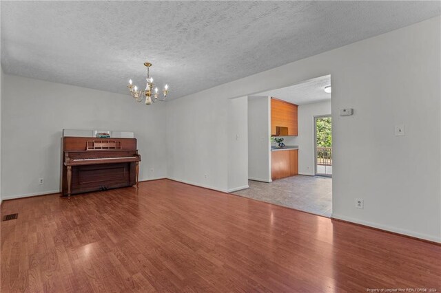 spare room featuring wood-type flooring, an inviting chandelier, and a textured ceiling