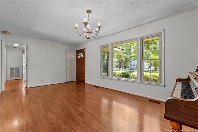 unfurnished room with a textured ceiling, wood-type flooring, and a notable chandelier